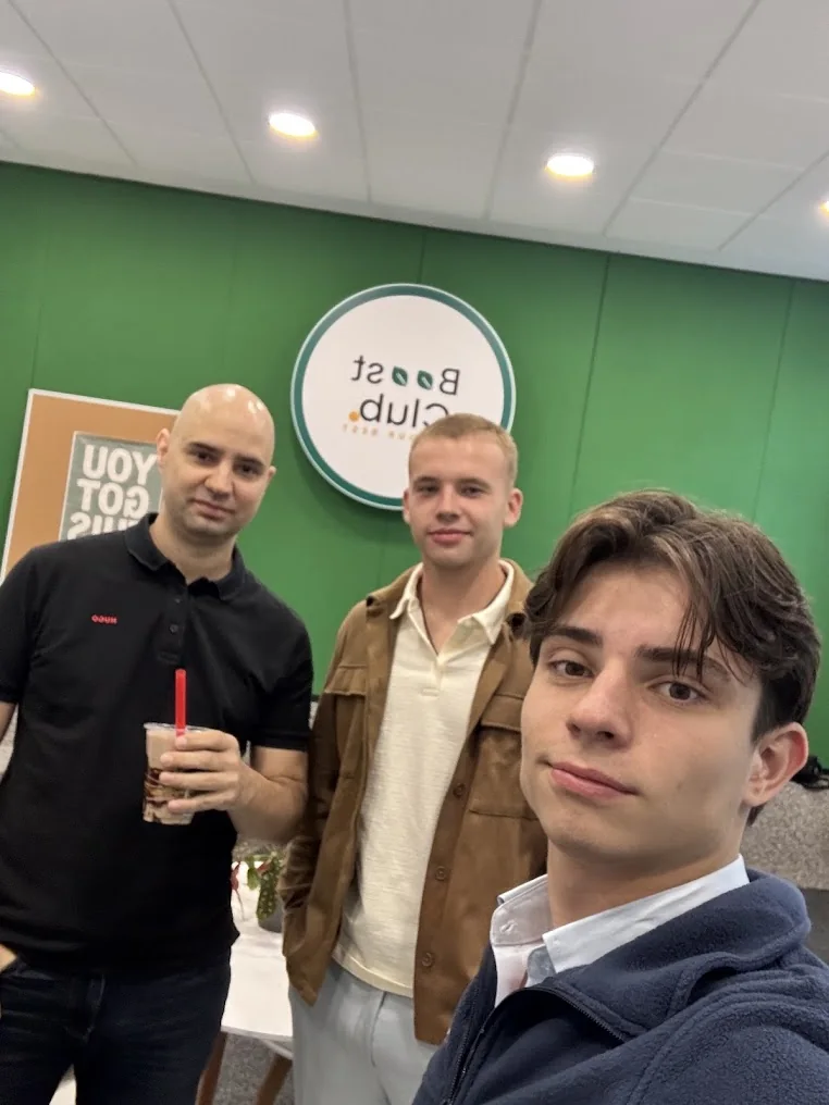 Trei oameni fotografiați în fața siglei Boost Club