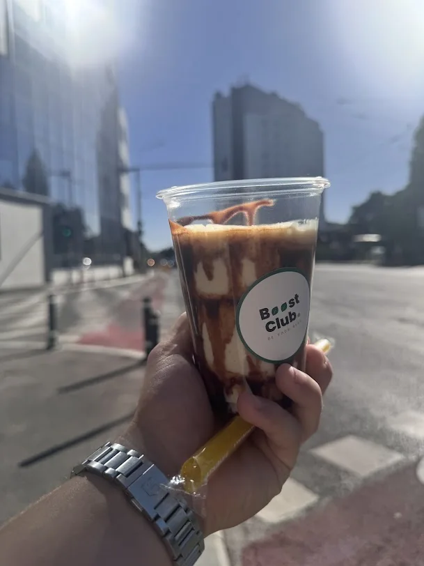 Un pahar Boost Club fotografiat afară, cu clădiri în fundal
