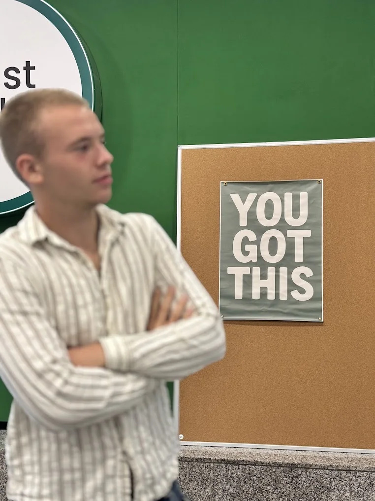 Un bărbat lângă peretele verde și un mesaj motivațional din Boost Club