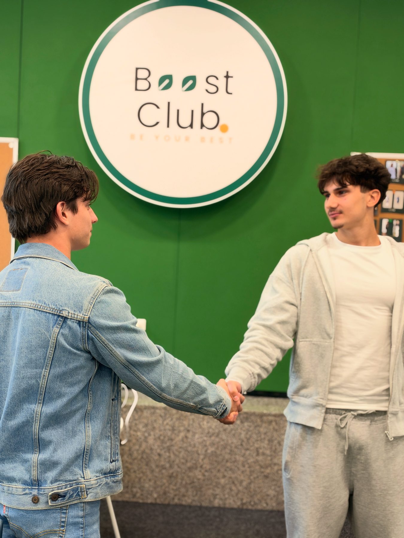 Two friends shaking hands under the Boost Club sign
